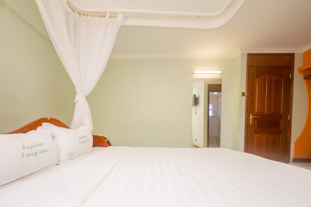 A bed with white bedding and a canopy, a wooden headboard, and a door to the right.