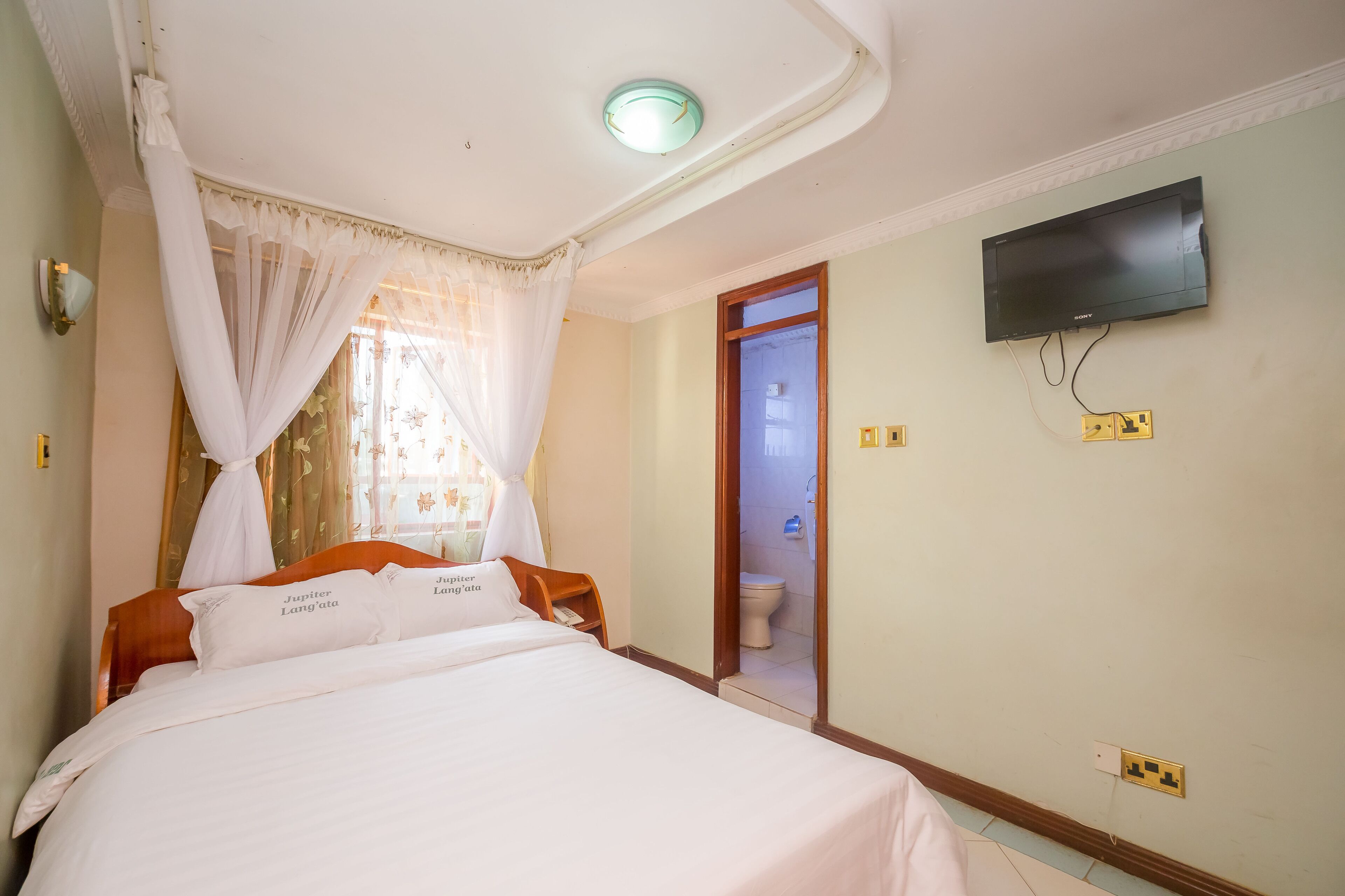 A hotel room with a bed, a television mounted on the wall, and a bathroom door.