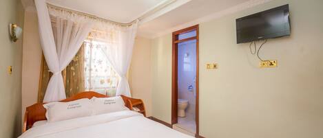 A hotel room with a bed, a television mounted on the wall, and a bathroom door.