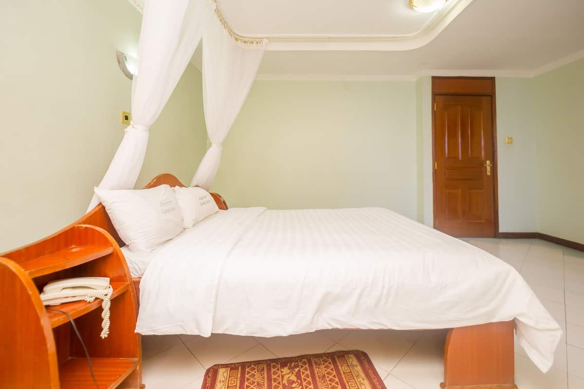 A bedroom with a bed, a wooden nightstand, a telephone, a white canopy, and a door.