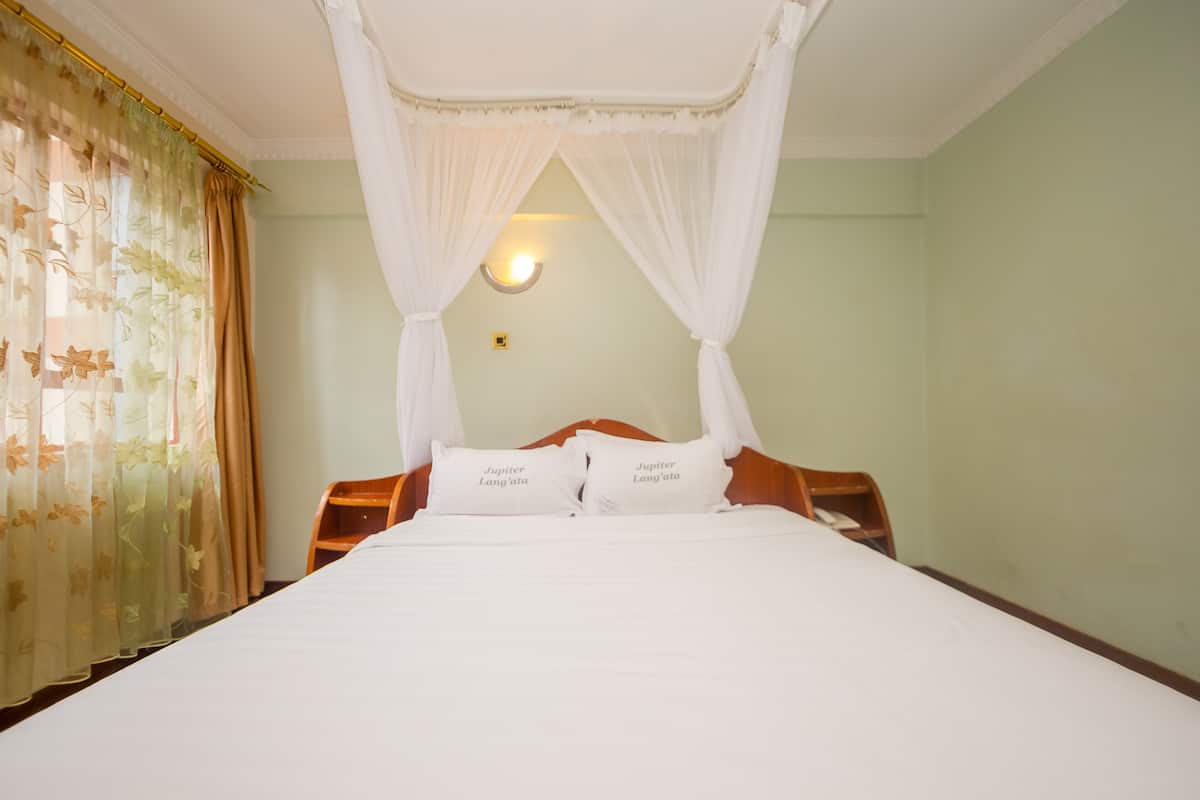 A room with a bed, a nightstand, a wall-mounted lamp, and a window with curtains.