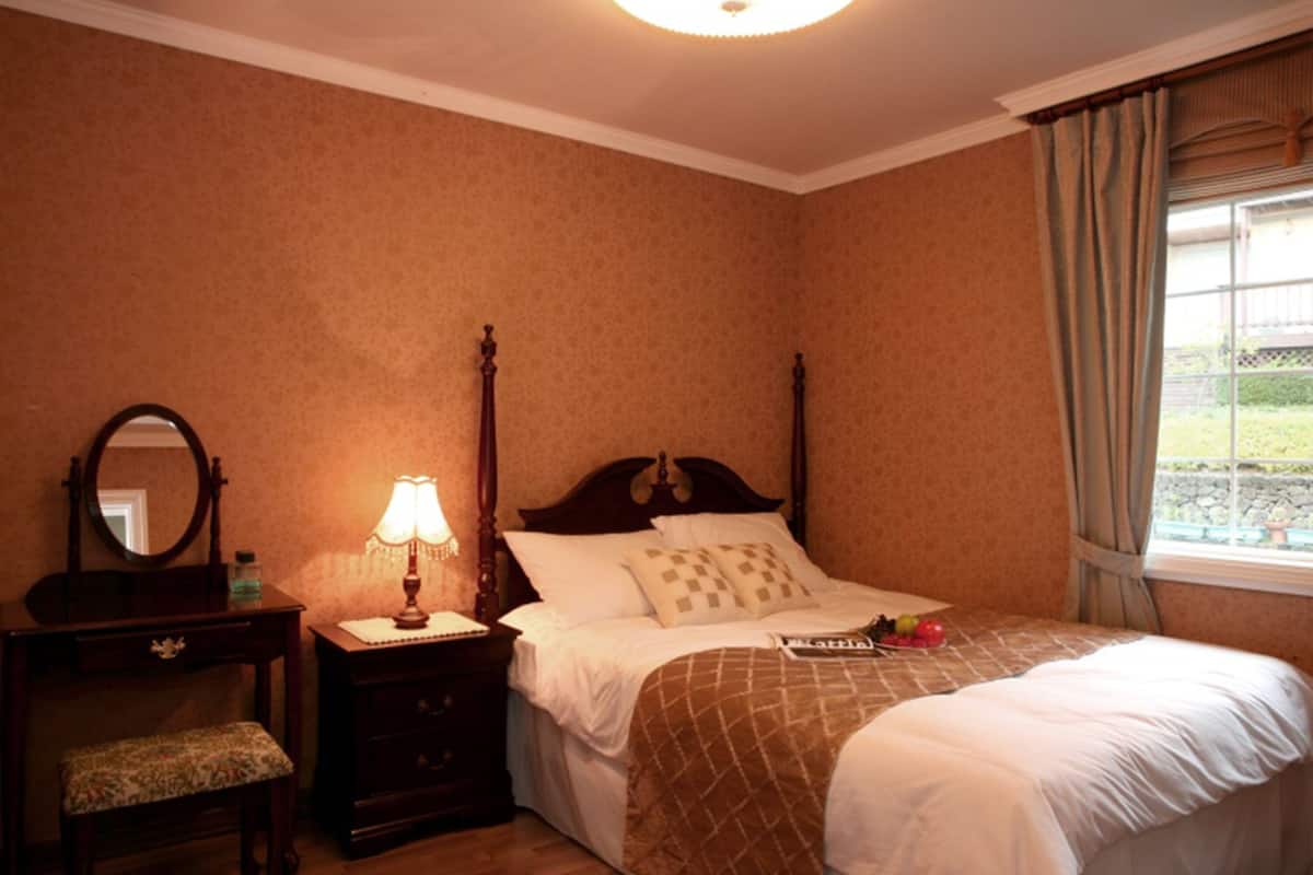 A bedroom with a bed, a nightstand with a lamp, a dresser, and a mirror.