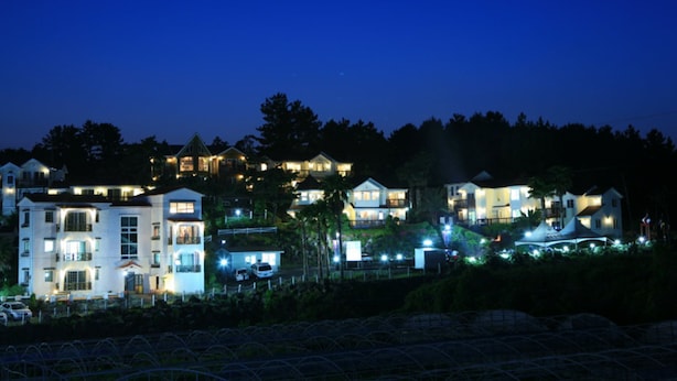 A coastal residential area with multiple houses at night, featuring well-lit exteriors and a clear view of the surrounding landscape. - Dasom Pension (Seogwipo)