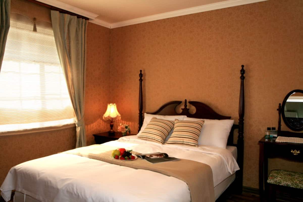 A neatly made bed with a fruit bowl, a bedside lamp, and a bedside table with a mirror.