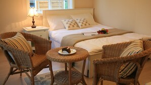 A neatly arranged bedroom with a bed, two wicker chairs, a small round table with a plate of food, and a bedside lamp. - Dasom Pension (Seogwipo)