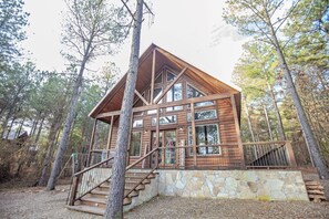 A log cabin with a stone foundation, large windows, and a staircase leading to the entrance.