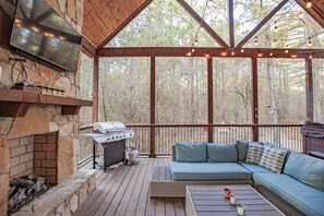 A covered outdoor area with a stone fireplace, a grill, and a cushioned seating area.