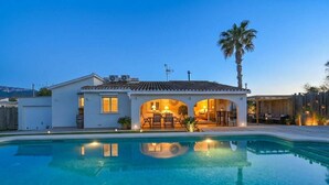 Une maison avec une piscine, un patio doté de mobilier d’extérieur et un palmier.