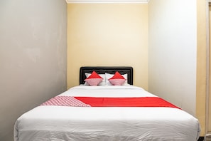 Habitación de hotel estrecha con cama, ropa de cama blanca y almohadas rojas.