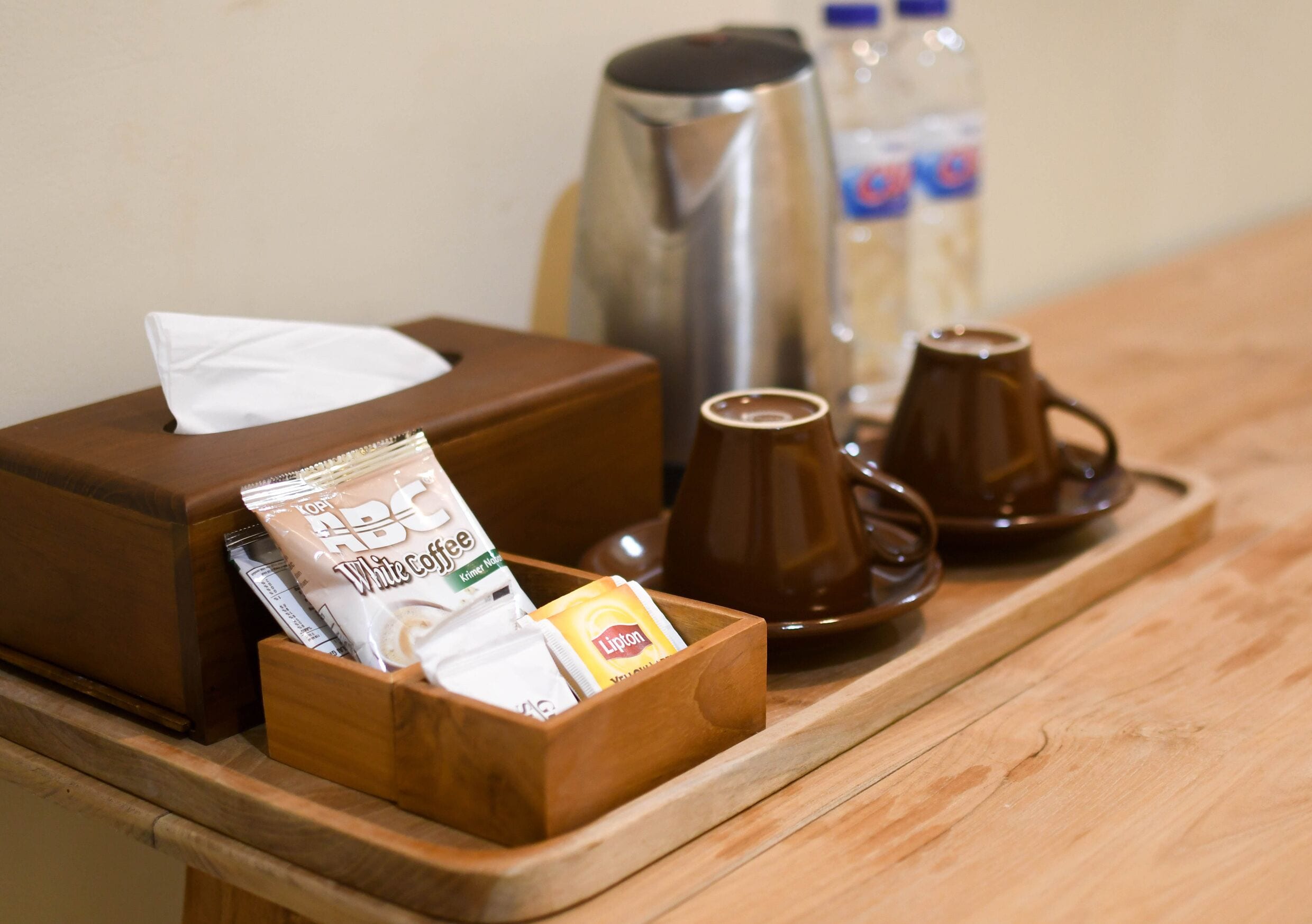 Ein Holztablett mit einer Taschentuchbox, einer Kaffeemaschine und zwei Tassen auf einem Holztisch.