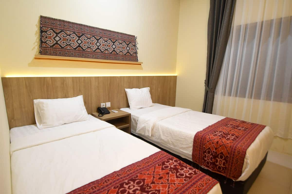 A hotel room with two beds, a wooden headboard, a patterned tapestry, and a curtain.