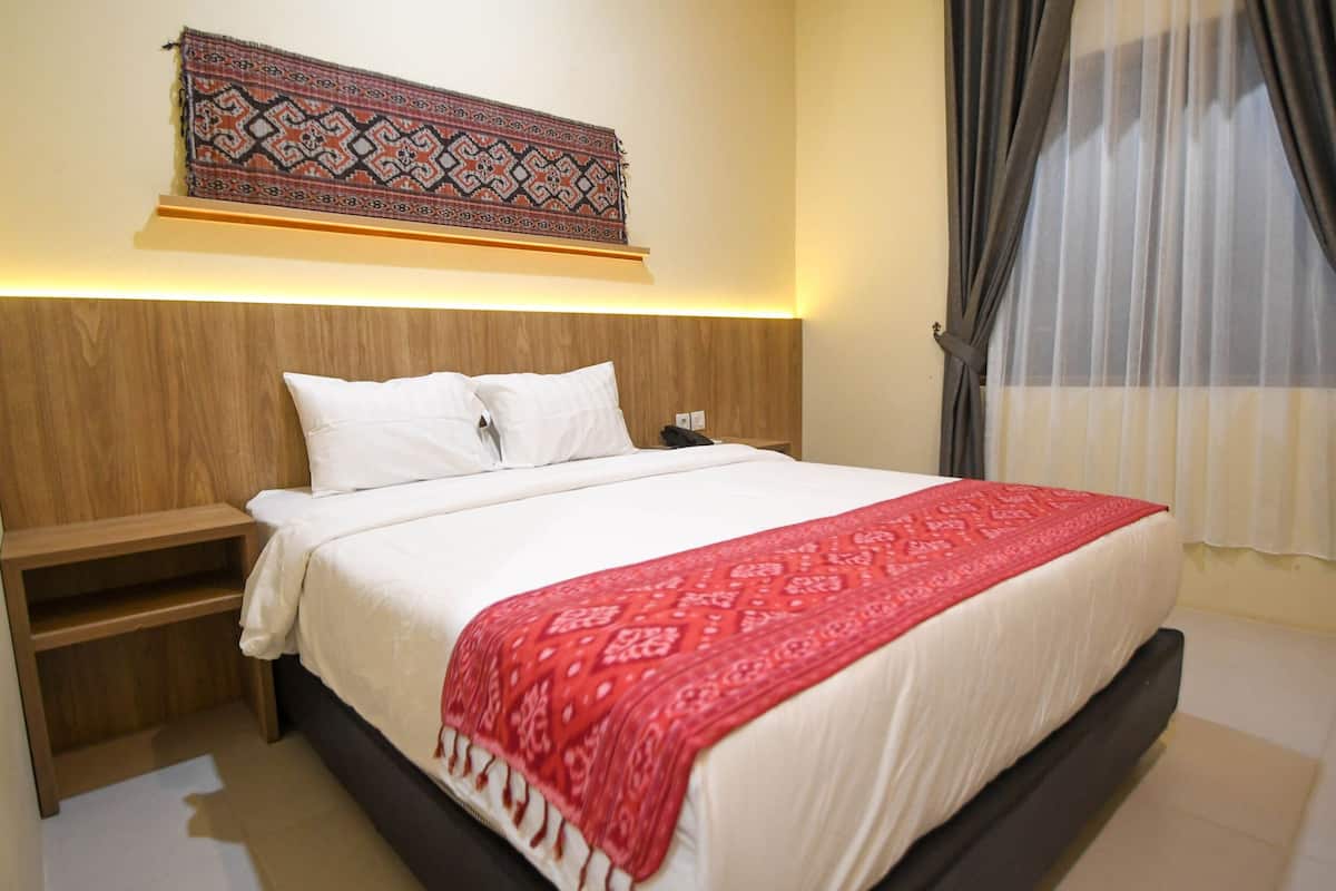 A neatly made bed with a red patterned throw, a wooden headboard, and a wall-mounted tapestry.