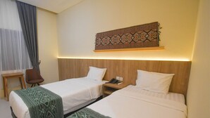 Habitación de hotel con dos camas individuales, cabecero de madera, tapiz estampado, una silla y una mesita de noche con teléfono.