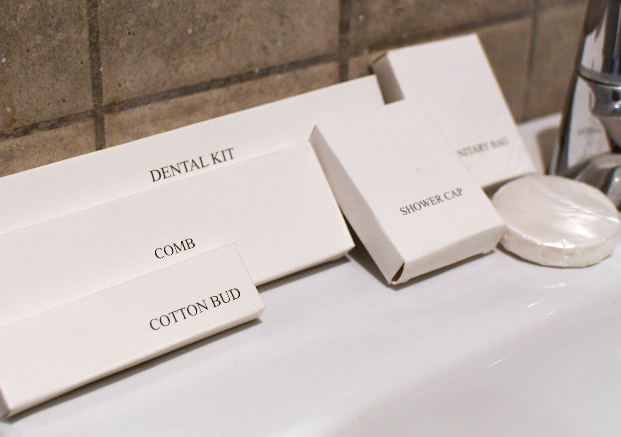 A bathroom with a white sink, a shower cap, and a dental kit.