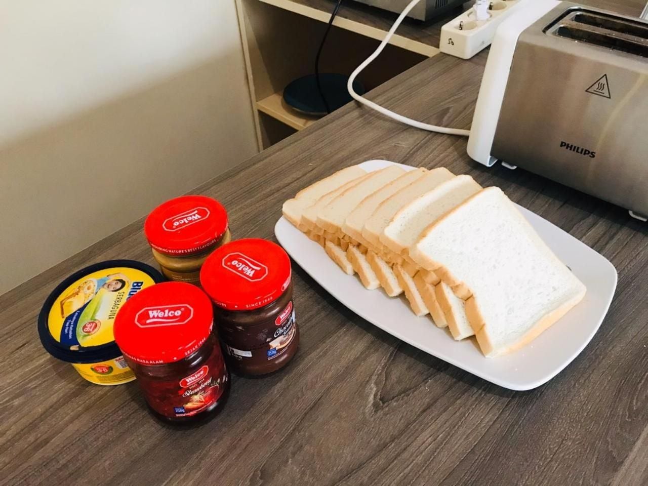 A table with a plate of sliced bread, two jars of jam, and a container of spread.