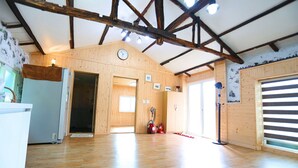 A spacious room with wooden floors, a ceiling with exposed beams, a clock on the wall, and a door leading to another room. - Doldam Path Pension (Seogwipo)