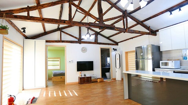 A spacious kitchen with wooden beams, a flat-screen TV, a refrigerator, and a microwave. - Doldam Path Pension (Seogwipo)