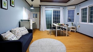Ein Wohnzimmer mit einem dunkelblauen Sofa, einem runden weißen Teppich und einem Essbereich mit einem weißen Tisch und Stühlen.