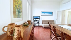 A dining area with a wooden table, chairs, a sofa, and a television on a stand. - Villa Porticciolo - Villa with a wonderful sea view in Rio Marina - ibookingelba (Rio Marina)