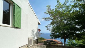 A white building with green shutters, a stone-paved entrance, and a view of the sea. - Villa Porticciolo - Villa with a wonderful sea view in Rio Marina - ibookingelba (Rio Marina)