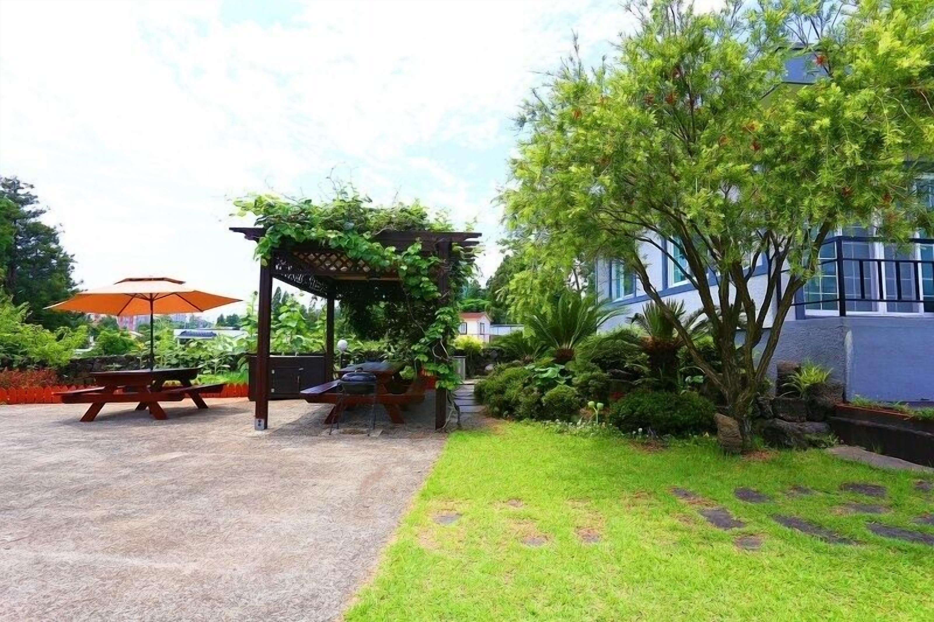 Un patio abrité avec une pergola en bois, des tables de pique-nique et un parasol.