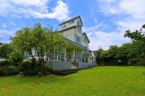 A modern two-story house with a large front lawn, a staircase leading to the entrance, and a well-maintained garden. - Munmoon House (Seogwipo)