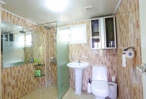 A bathroom with a glass shower enclosure, a white sink, a toilet, and a small shelf with toiletries. - Munmoon House (Seogwipo)