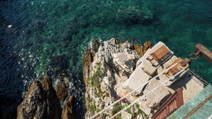 A coastal cliff with clear water, rocky terrain, and a wooden structure with seating. - Apartments Hinterreiter (Rovinj)