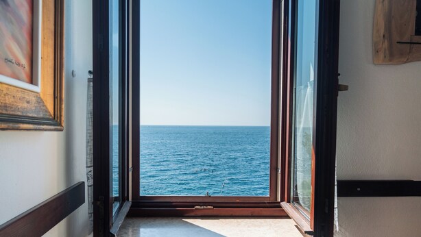 A view through a window to the sea, with a wooden floor and a framed picture on the wall. - Apartments Hinterreiter (Rovinj)