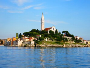 Une ville côtière avec une église imposante située sur une colline, entourée de bâtiments résidentiels et bordée par une étendue d’eau.