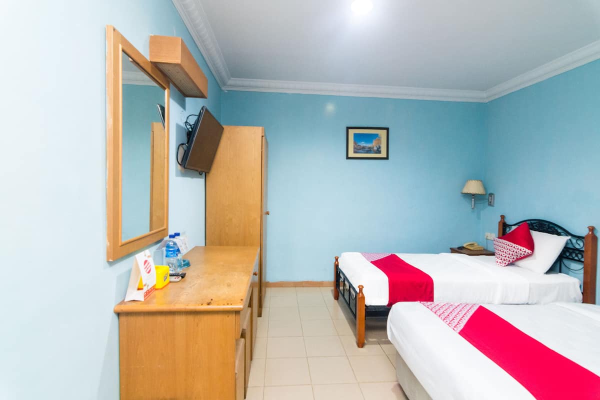 Een hotelkamer met twee bedden, een houten bureau, een spiegel, een televisie en een klein schilderij aan de muur.