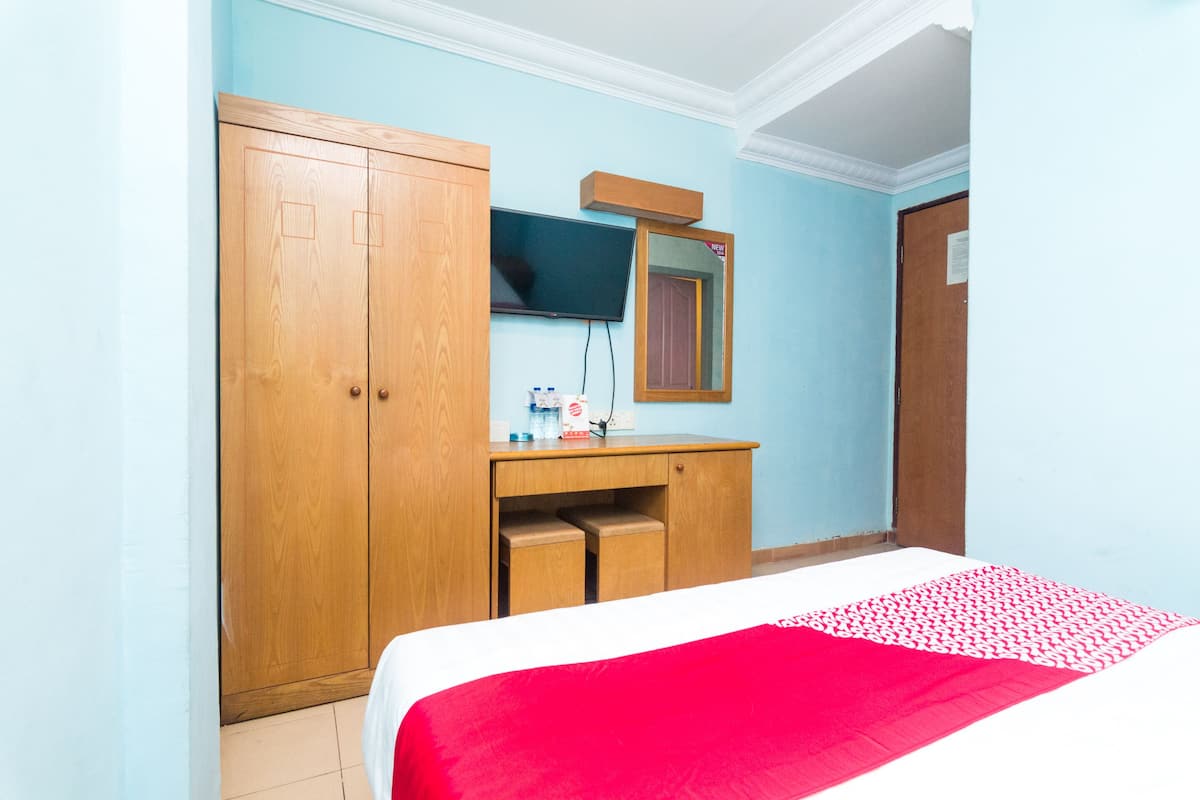 Een slaapkamer met een bed, een houten garderobe, een bureau met spiegel en een televisie aan de muur.