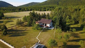 Une maison entourée d’un vaste champ verdoyant et d’arbres, sous un ciel dégagé.