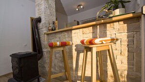 Une pièce avec un mur en pierre, un tabouret en bois, un radiateur noir et une étagère sur laquelle se trouve une plante.