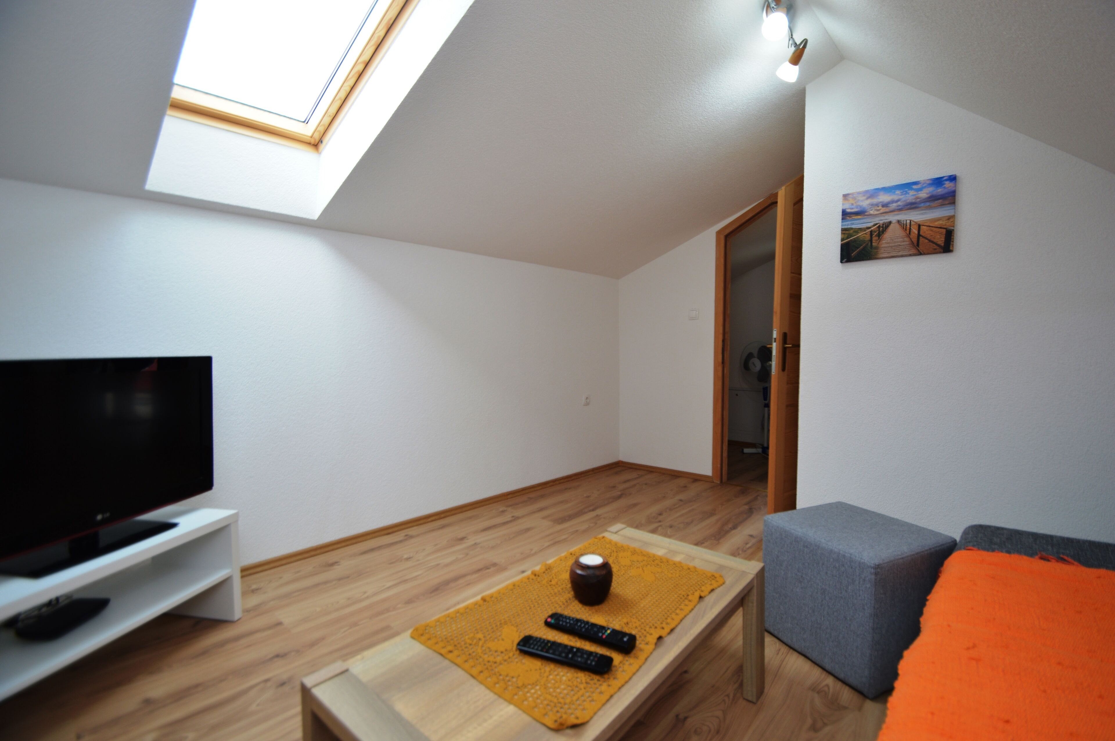 Een moderne woonkamer met dakraam, een flatscreen televisie, een houten salontafel met afstandsbedieningen en een grijze bank.