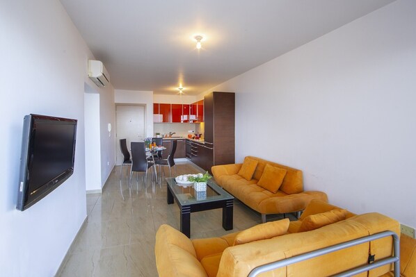 Een moderne woonkamer met een flatscreen televisie, een zithoek en een eethoek met een tafel en stoelen.