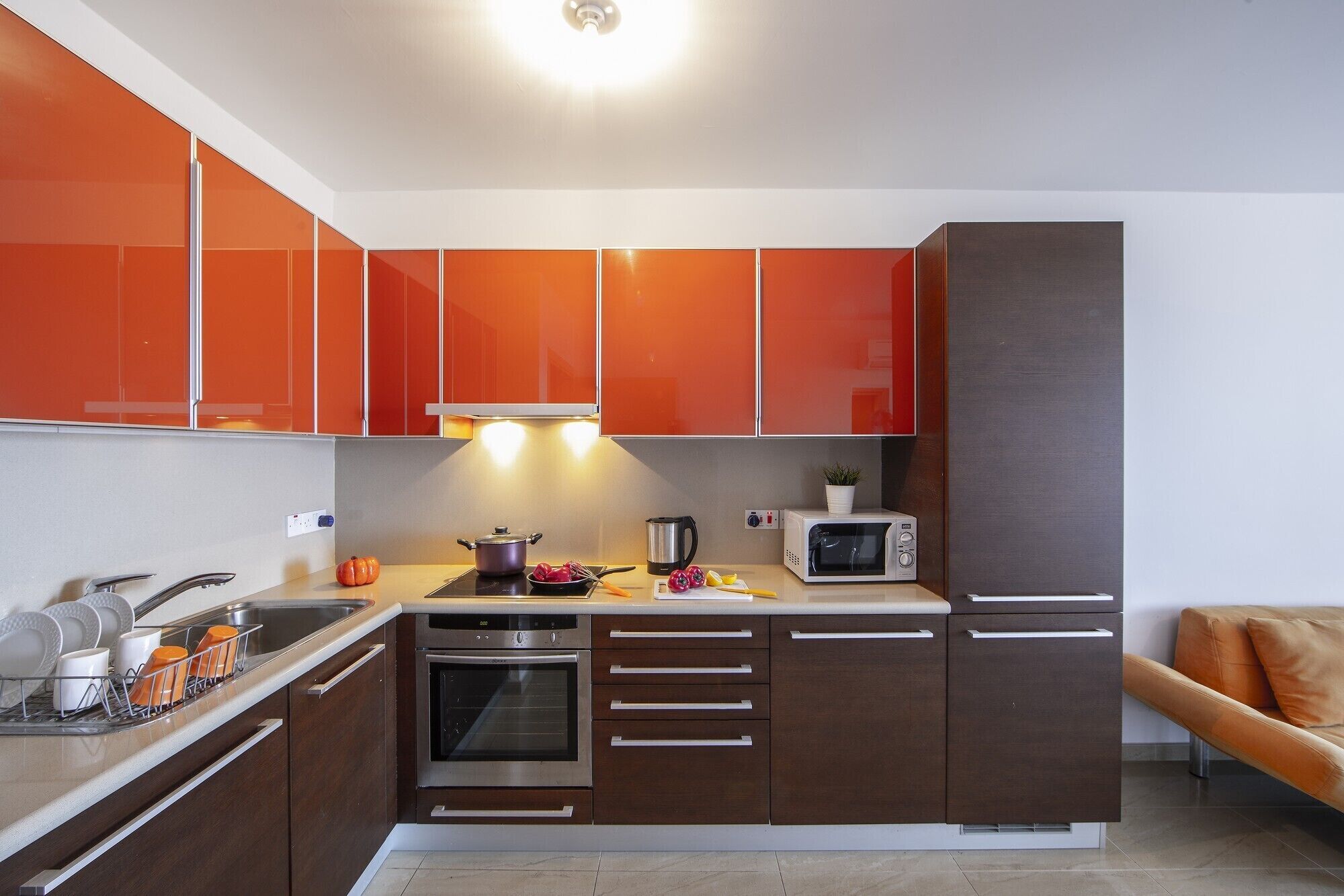 Una cocina moderna con armarios color naranja, horno empotrado, microondas y un lavabo.