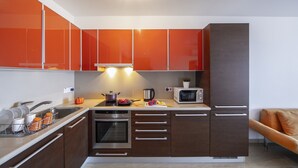 A modern kitchen with orange cabinets, a built-in oven, a microwave, and a sink. - 1 Bedroom apartment located in the heart of protaras. (Protaras)