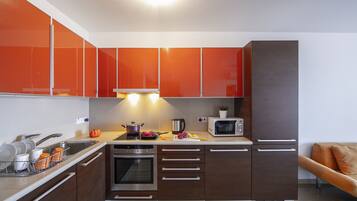 Una cocina moderna con armarios color naranja, horno empotrado, microondas y un lavabo.