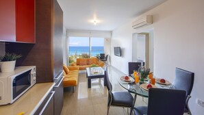 A modern living room with a sofa, a dining table with chairs, a TV, and a view of the ocean. - 1 Bedroom apartment located in the heart of protaras. (Protaras)