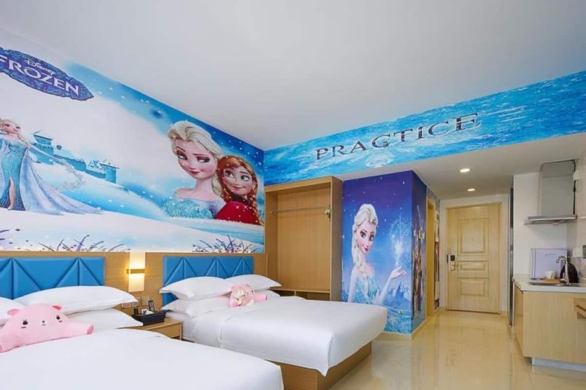 A hotel room with two beds, a mural of Frozen characters, and a 'PRACTICE' sign on the wall.