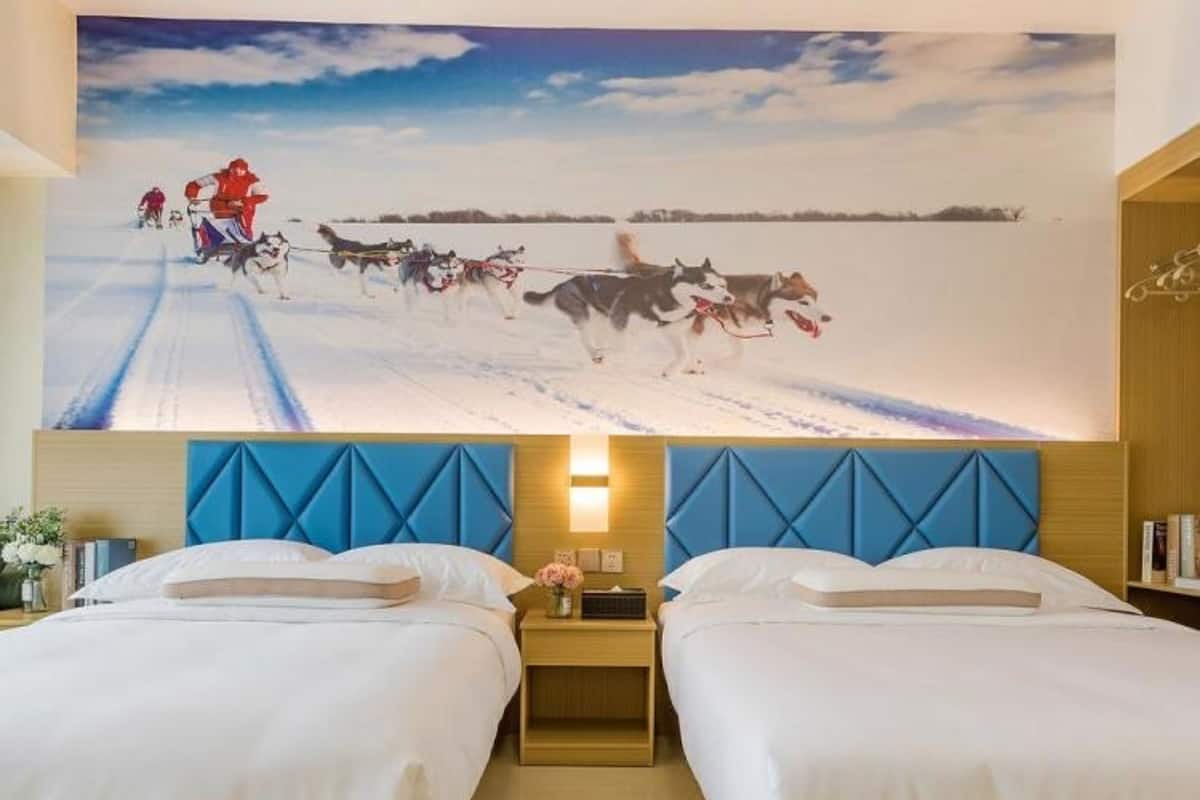 A hotel room with two beds, a large wall mural of sled dogs, and a blue headboard.