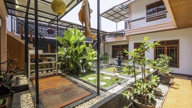Une cour spacieuse avec une terrasse en bois, des plantes en pot et une sculpture de poisson suspendue.