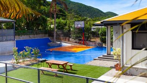 A pool area with a basketball court, palm trees, and a mountain in the background. - Regina Ishigaki Kabira Sky (Ishigaki)