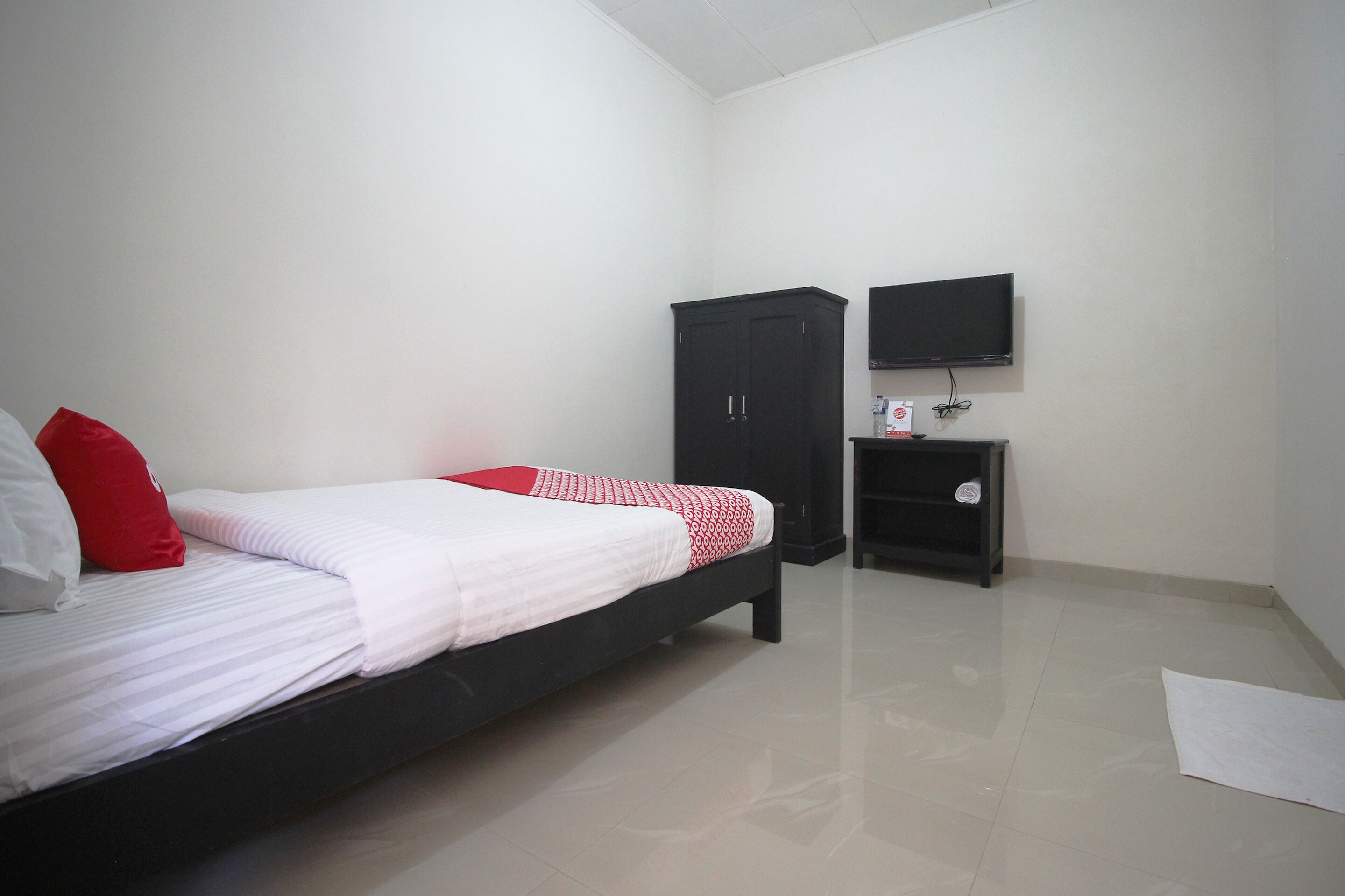 A bedroom with a bed, a wardrobe, a TV, and a small shelf.