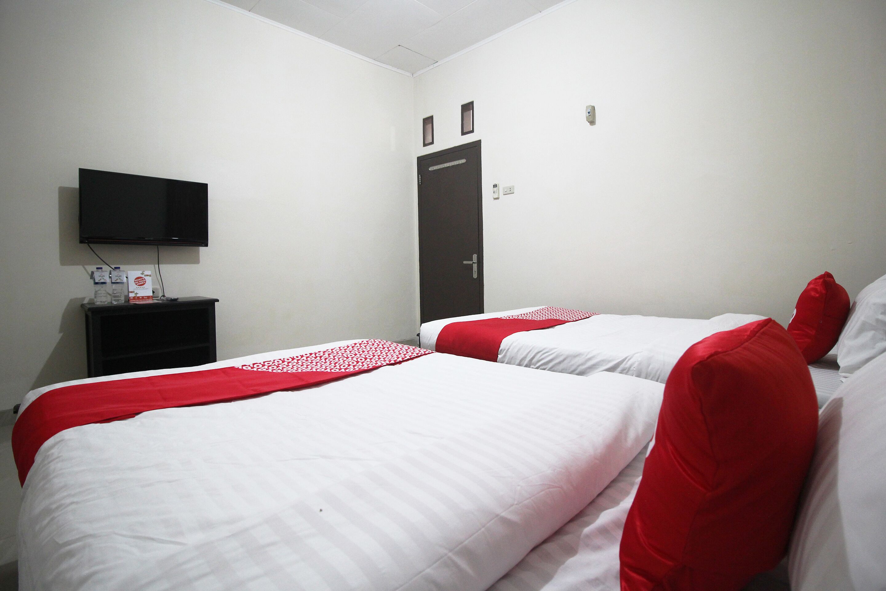 A hotel room with two beds, a TV mounted on the wall, and a door with a handle.