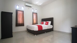 A bedroom with a bed, a wardrobe, and two windows with curtains. - Hotel O Wisma Ray Syariah (Bandar Lampung)