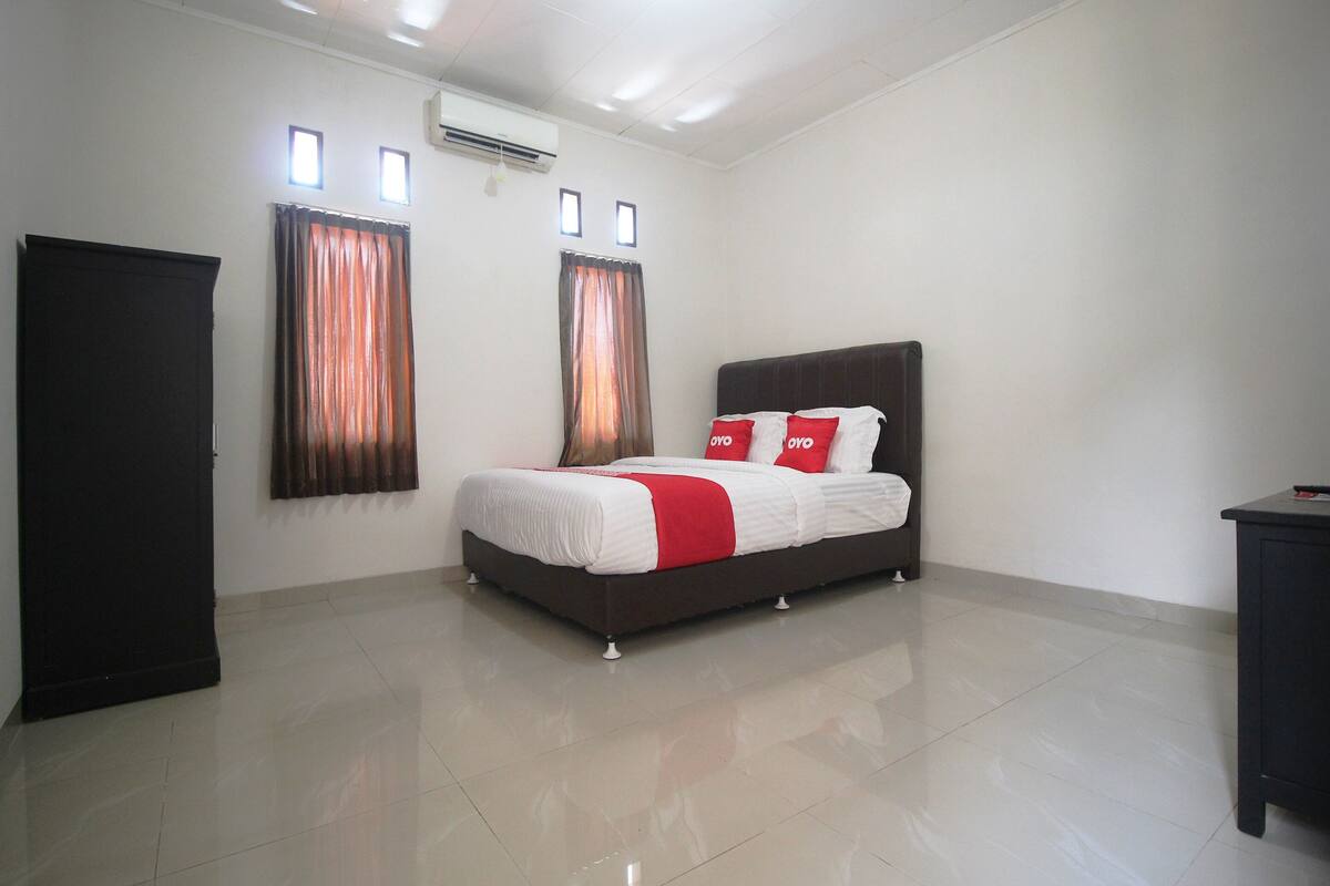 Un dormitorio con cama, armario y dos ventanas con cortinas.