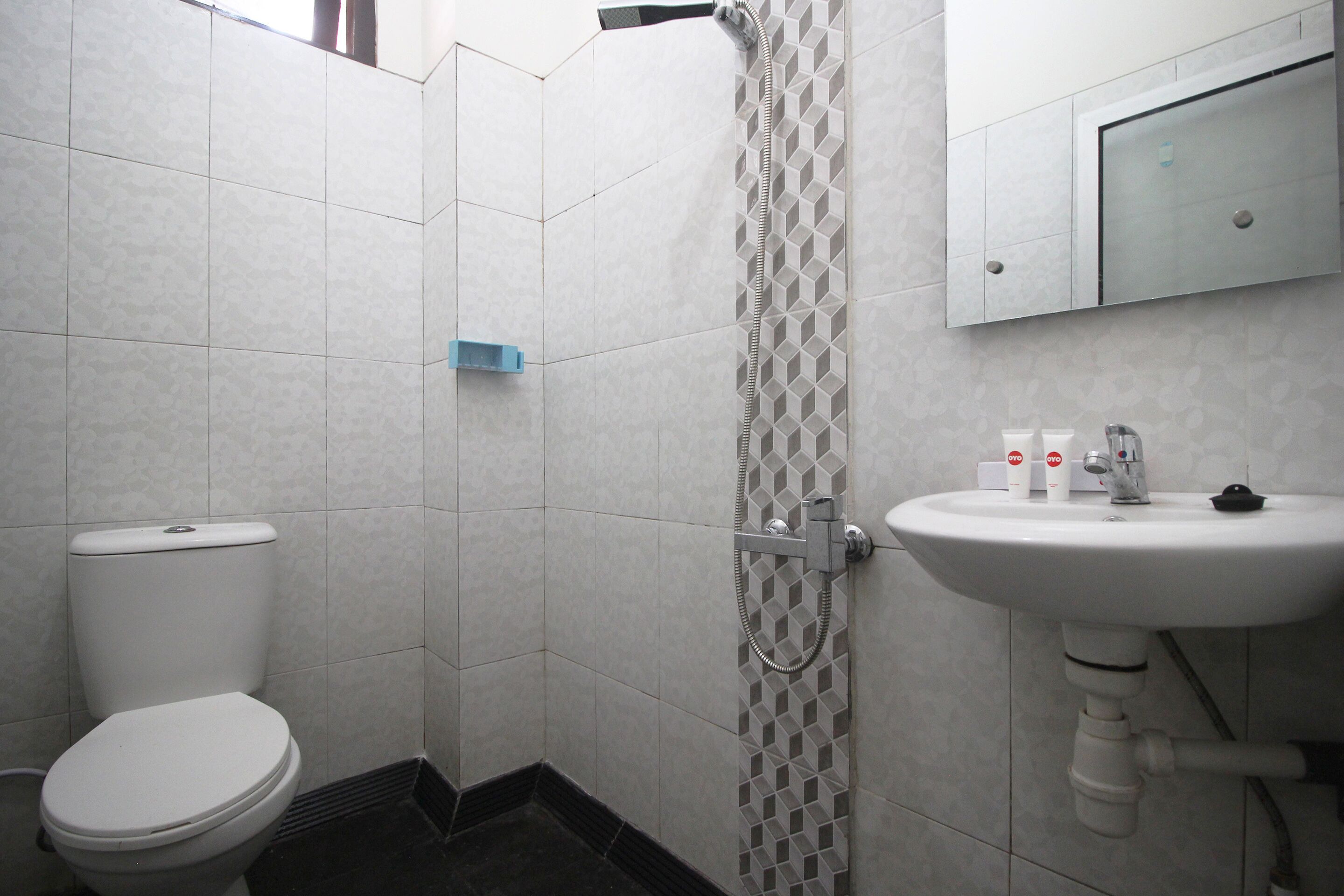 A bathroom with a toilet, a shower with a geometric tile pattern, and a sink with a mirror above it.