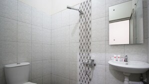 A bathroom with a toilet, a shower with a geometric tile pattern, and a sink with toiletries. - Hotel O Wisma Ray Syariah (Bandar Lampung)